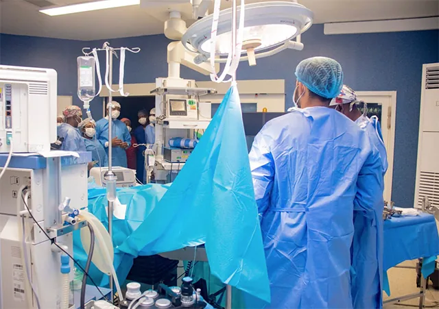 Two surgeons in blue scrubs in the operating theatre, in front of an operating table and an anaesthesia machine