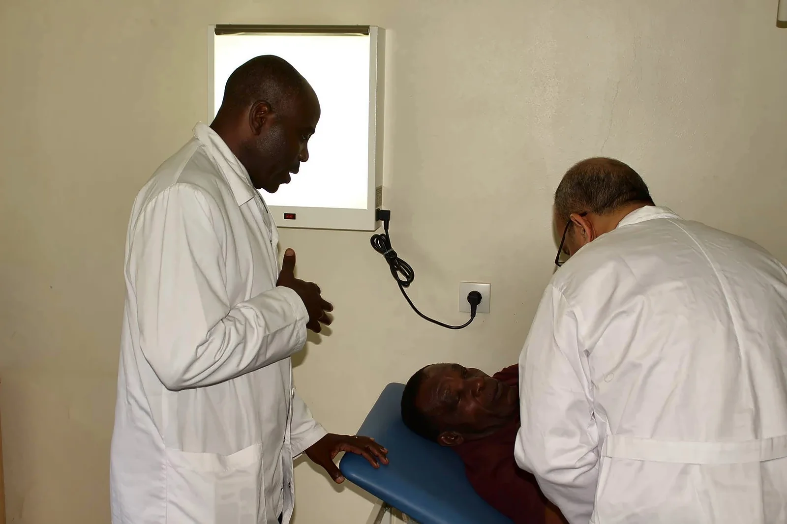 Consultation de neurochirurgie lors de la mission au CHU d’Agondjé, au Gabon : deux médecins examinent un patient allongé.