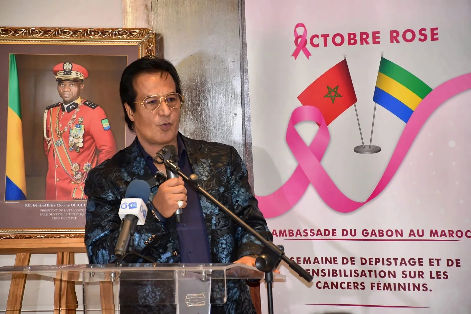 Speech at the lectern during a Pink October day, in front of a visual with the flags of Morocco and Gabon