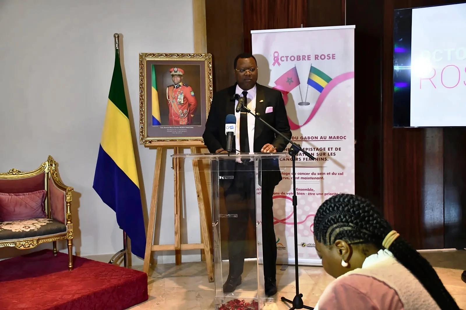 Second speech at the lectern in front of the Pink October campaign visual and the flags
